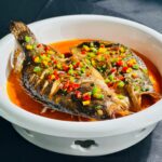 Traditional spicy fish dish served with colorful peppers in a white bowl.